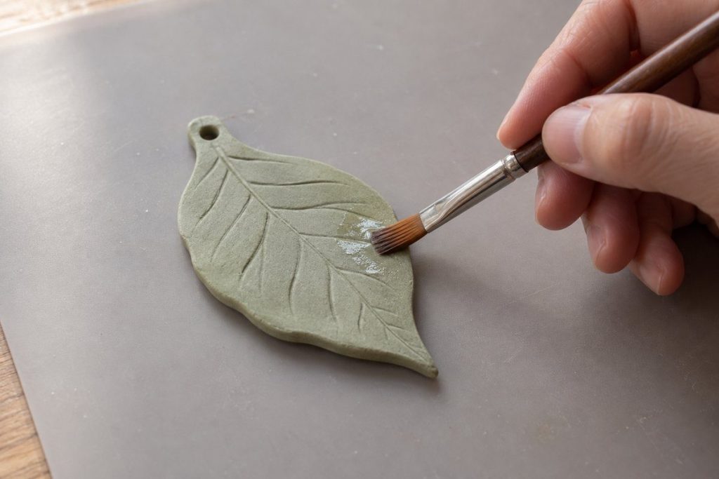 葉形の粘土作品に筆で透明な仕上げ材を塗る制作イメージ